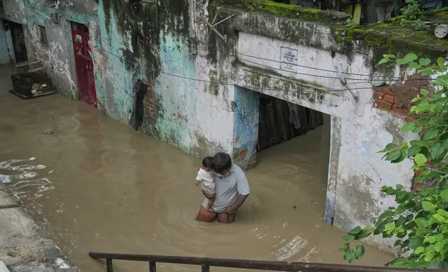 A resident carries his son and wades through floodwater after the river Yamuna, swollen by incessant rain in the higher regions, overran its banks, in New Delhi, India, Tuesday, Sept. 2, 2025. (AP Photo/Manish Swarup)
