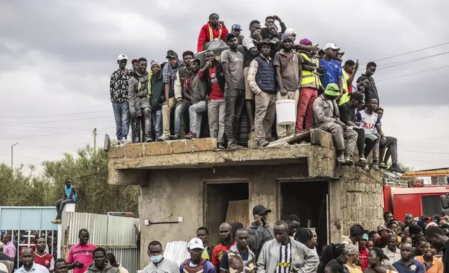 People gather near the site of an airplane belonging to the African Medical and Research Foundation (AMREF) that crashed into a residential building in the Mwihoko area of Ruiru, Kenya, Aug. 7, 2025. (AP Photo/Samson Otieno)