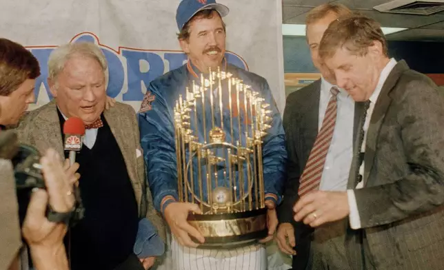 FILE - New York Mets Manager Davey Johnson, center, holds baseball's World Series trophy on the podium after the Mets defeated the Boston Red Sox in Game 7, at Shea Stadium in New York, Oct. 27, 1986. Mets General Manager Frank Cashen, left, Baseball Commissioner Peter Ueberroth, partially hidden, and Mets President Fred Wilpon, right, join the celebration in the locker room the clubhouse. (AP Photo/Ray Stubblebine, File)