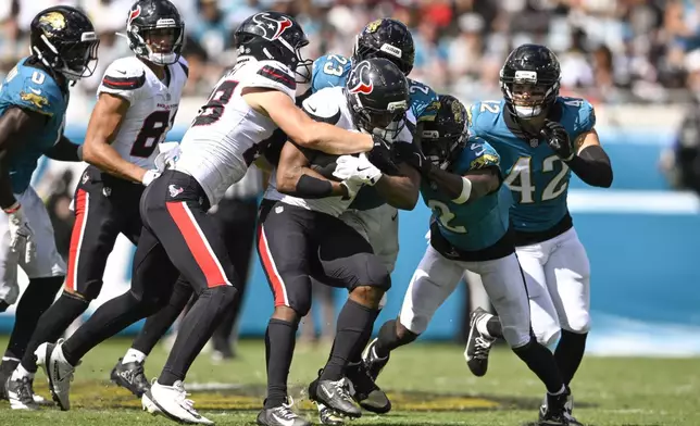 Houston Texans running back Nick Chubb, center, is stopped by Jacksonville Jaguars linebacker Foye Oluokun (23), cornerback Jourdan Lewis (2) and safety Andrew Wingard (42) during the second half of an NFL football game Sunday, Sept. 21, 2025, in Jacksonville, Fla. (AP Photo/Phelan M. Ebenhack)