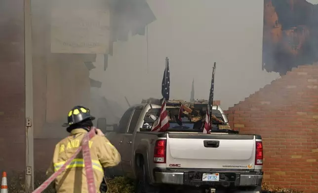 A vehicle that was rammed into the building is surrounded by smoke as a firefighter works on the scene at the Church of Jesus Christ of Latter-day Saints in Grand Blanc, Mich., Sunday, Sept. 28, 2025. (Lukas Katilius/The Flint Journal via AP)