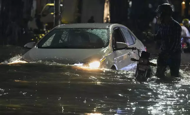 People in car drive and a motorcyclist pushes is vehicle through a flooded road caused by heavy rain in Lahore, Pakistan, Monday, Sept. 8, 2025. (AP Photo/K.M. Chaudary)