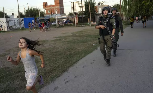 FILE PHOTO GALLERY - A girl runs past as border police agents patrol Los Pumitas neighborhood, where an 11-year-old boy was killed days earlier when at least one gunmen attacked a birthday party, amid escalating drug violence in Rosario, Argentina, March 9, 2023. (AP Photo/Rodrigo Abd)