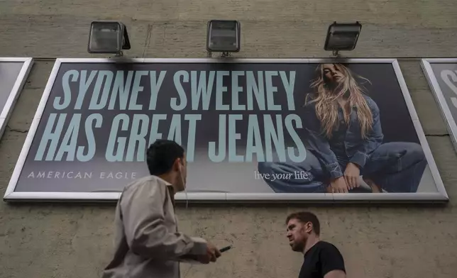 FILE - People walk past a campaign poster starring Sydney Sweeney which is displayed at the American Eagle Outfitters store, Friday, Aug. 1, 2025, in New York. (AP Photo/Yuki Iwamura, File)