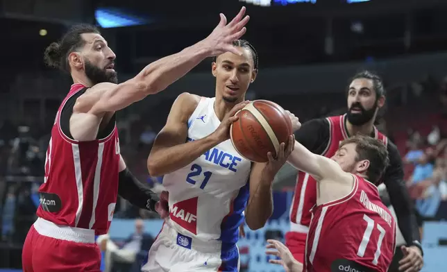 France's Zaccharie Risacher, centre, drives between Georgia's Tornike Shengelia, left, and Georgia's Giorgi Ochkhikidze during the Eurobasket, European Basketball Championship round of 16 match between France and Georgia at the Riga Arena in Riga, Latvia, Sunday, Sept. 7, 2025. (AP Photo/Sergei Grits)