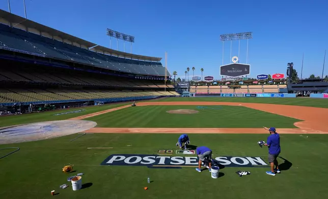 Los Angeles Dodgers grounds crew members paint the "Postseason" logo on the field at Dodger Stadium prior to baseball practice Monday, Sept. 29, 2025, in Los Angeles ahead of the Wild Card Series between the Dodgers and the Cincinnati Reds. (AP Photo/Mark J. Terrill)