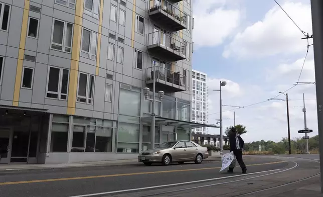 A worker walks to pick up litter while carrying a sign left outside the U.S. Immigration and Customs Enforcement building close by in Portland, Ore., on Tuesday, Sept. 9, 2025. (AP Photo/Jenny Kane)