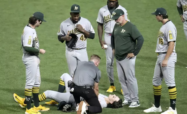 Athletics manager Mark Kotsay, second from right, watches as Zack Gelof, bottom, is tended to by a team trainer during the fifth inning of a baseball game against the Pittsburgh Pirates in Pittsburgh, Friday, Sept. 19, 2025. (AP Photo/Gene J. Puskar)