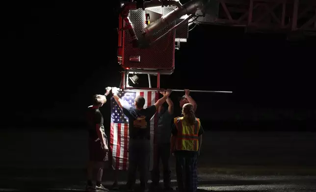Firefighters attach an American flag to a firetruck before a procession after multiple police officers were shot and killed Wednesday, Sept. 17, 2025, in Spring Grove, Pa. (AP Photo/Matt Slocum)