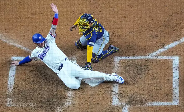 Texas Rangers' Jonah Heim, bottom, slides in to score ahead of the tag of Milwaukee Brewers catcher William Contreras on a double by Rangers' Michael Helman during the seventh inning of a baseball game Monday, Sept. 8, 2025, in Arlington, Texas. (AP Photo/Julio Cortez)