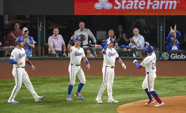 Texas Rangers' Michael Helman, right, is greeted near home plate by teammates, from left, Jonah Heim, Dylan Moore and Kyle Higashioka after scoring them all on a grand slam off Milwaukee Brewers starting pitcher Jose Quintana during the fifth inning of a baseball game Monday, Sept. 8, 2025, in Arlington, Texas. (AP Photo/Julio Cortez)