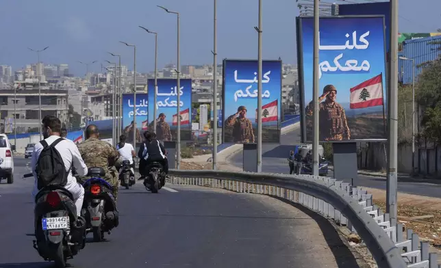 People on scooters drive past billboards in support of the Lebanese army with Arabic reading: "We are all with you," set up on the highway leading to Beirut international airport, in Beirut, Lebanon, Sept. 3, 2025. (AP Photo/Hussein Malla)
