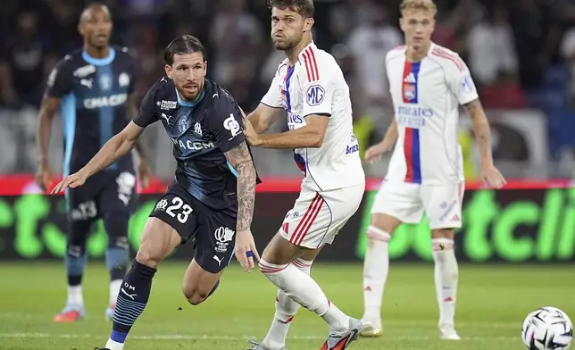 Marseille's Pierre-Emile Hojbjerg, left, challenges for the ball with Lyon's Francis Tessmann during the French League One soccer match between Lyon and Marseille, in Decines, outside Lyon, France, Sunday, Aug. 31, 2025. (AP Photo/Laurent Cipriani)