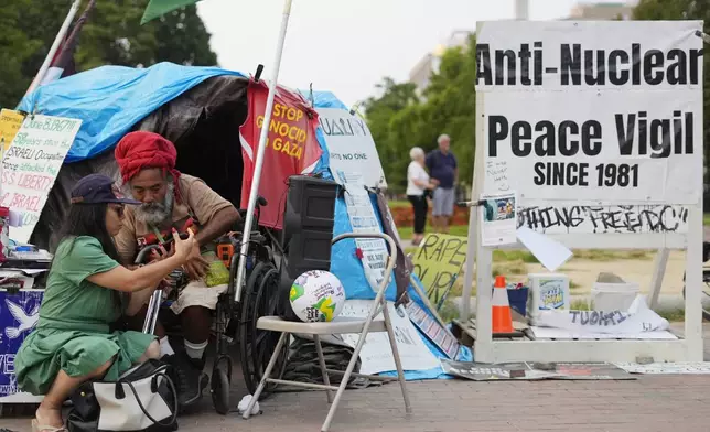 Philipos Melaku-Bello, second from left, looks over a passerbys phone while at the White House Peace Vigil in Lafayatte Park across the street from the White House in Washington, Friday, Sept. 5, 2025. (AP Photo/Pablo Martinez Monsivais)