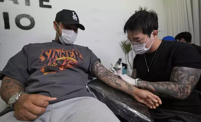 Tattoo artist Song Jaemin, right, works to tattoo an image of Jesus Christ on the forearm of Lee Byong-joo at his studio in Goyang, South Korea, Thursday, Sept. 18, 2025. (AP Photo/Ahn Young-joon)