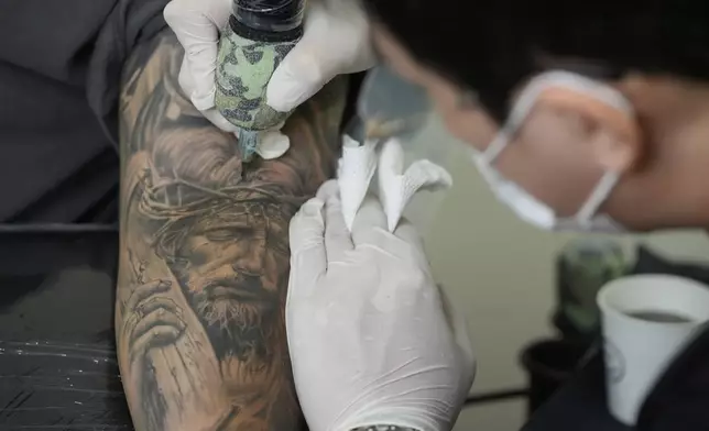Tattoo artist Song Jaemin, right, works to tattoo an image of Jesus Christ on the forearm of Lee Byong-joo at his studio in Goyang, South Korea, Thursday, Sept. 18, 2025. (AP Photo/Ahn Young-joon)