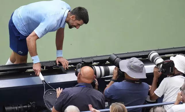 Novak Djokovic, of Serbia, runs into the photgraphers box against Carlos Alcaraz, of Spain, during the men's singles semifinals of the U.S. Open tennis championships, Friday, Sept. 5, 2025, in New York. (AP Photo/Frank Franklin)