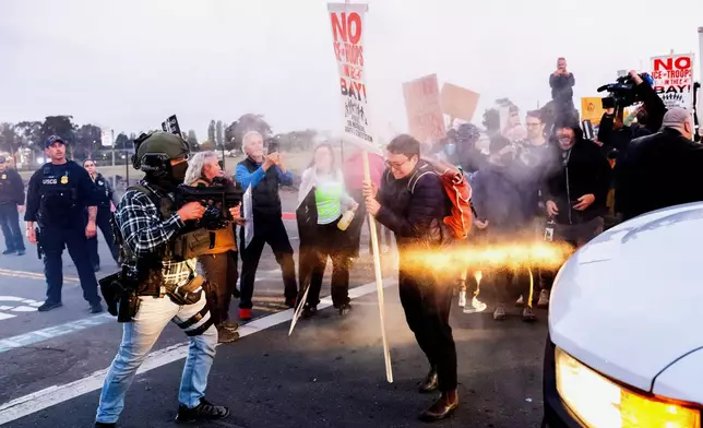 A person clears protesters blocking a caravan of U.S. Customs and Border Protection personnel trying to enter Coast Guard Base Alameda on Thursday, Oct. 23, 2025, in Oakland, Calif. (AP Photo/Noah Berger)