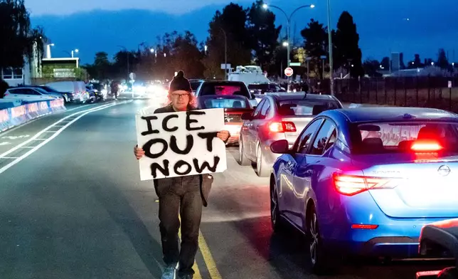A protester holds a sign while fellow demonstrators block traffic to Coast Guard Base Alameda on Thursday, Oct. 23, 2025, in Oakland, Calif. (AP Photo/Noah Berger)