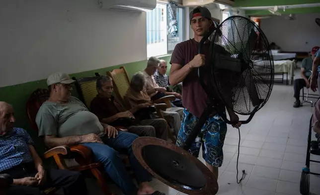 FILE - Humanitarian worker Roger Duvan Lagunes carries a fan into Cogra, an elderly shelter, in Veracruz, Mexico, on June 16, 2024. (AP Photo/Felix Marquez)