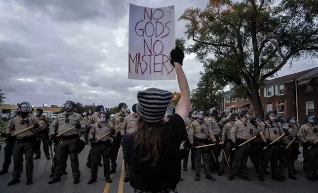 A demonstrator holds a sign as Illinois State Police move the crowd back after declaring an unlawful assembly outside the U.S. Immigration and Customs Enforcement facility in Broadview, Ill., Saturday, Oct. 11, 2025. (AP Photo/Adam Gray)