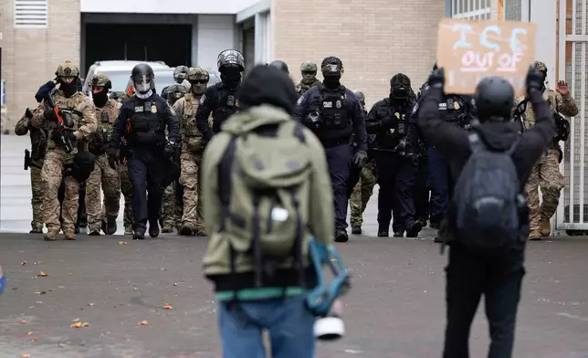 People protest outside a U.S. Immigration and Customs Enforcement facility as law enforcement officers walk out of the gates to guard vehicles leaving the facility on Saturday, Oct. 11, 2025, in Portland, Ore. (AP Photo/Jenny Kane)