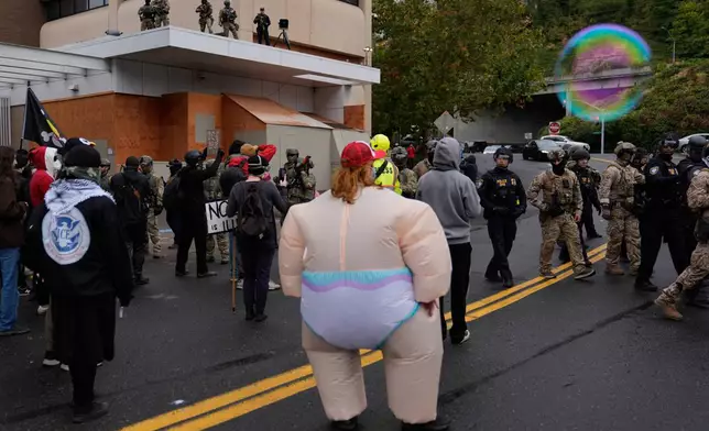 People protest as law enforcement stand in the street to allow vehicles to leave a U.S. Immigration and Customs Enforcement facility on Saturday, Oct. 11, 2025, in Portland, Ore. (AP Photo/Jenny Kane)