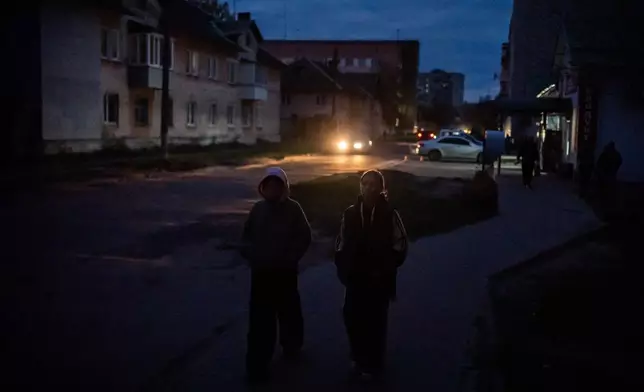 Kids walk along a dark residential street during a rolling blackout, Thursday, Oct. 16, 2025, in Shostka, Ukraine. (AP Photo/Julia Demaree Nikhinson)
