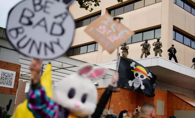 Law enforcement officers watch from the ledge of a U.S. Immigration and Customs Enforcement facility as people protest on Saturday, Oct. 11, 2025, in Portland, Ore. (AP Photo/Jenny Kane)