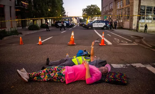 People relax on a street outside a U.S. Immigration and Customs Enforcement facility on Tuesday, Oct. 7, 2025, in Portland, Ore. (AP Photo/Ethan Swope)