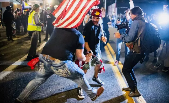 A Trump supporter, center, scuffles with a protester over a burning U.S. flag during a protest outside a U.S. Immigration and Customs Enforcement facility in Portland, Ore., Monday, Oct. 6, 2025. (AP Photo/Ethan Swope)