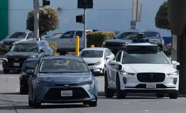 A Waymo vehicle, right, drives in San Bruno, Calif., Tuesday, Sept. 30, 2025. (AP Photo/Jeff Chiu)