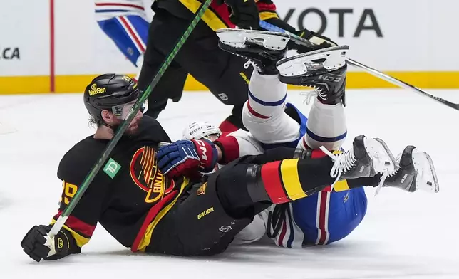 Vancouver Canucks' Marcus Pettersson, front left, and Montreal Canadiens' Zack Bolduc, right, fall to the ice after colliding during the second period of an NHL hockey game in Vancouver, British Columbia, Saturday, Oct. 25, 2025. (Darryl Dyck/The Canadian Press via AP)