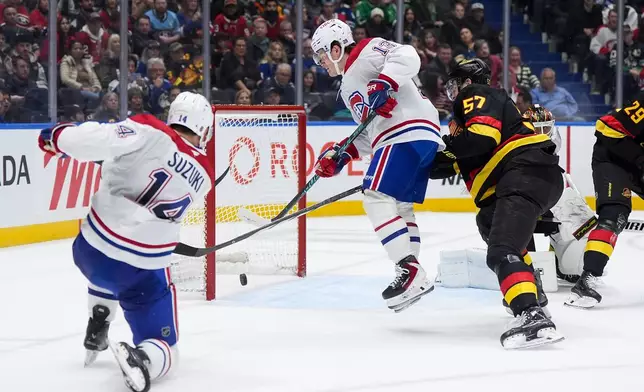 Montreal Canadiens' Nick Suzuki (14) scores into the open net behind Vancouver Canucks goalie Kevin Lankinen, back right, as Montreal's Cole Caufield (13) jumps in front of Vancouver's Tyler Myers (57) during the second period of an NHL hockey game in Vancouver, on Saturday, Oct. 25, 2025. (Darryl Dyck/The Canadian Press via AP)