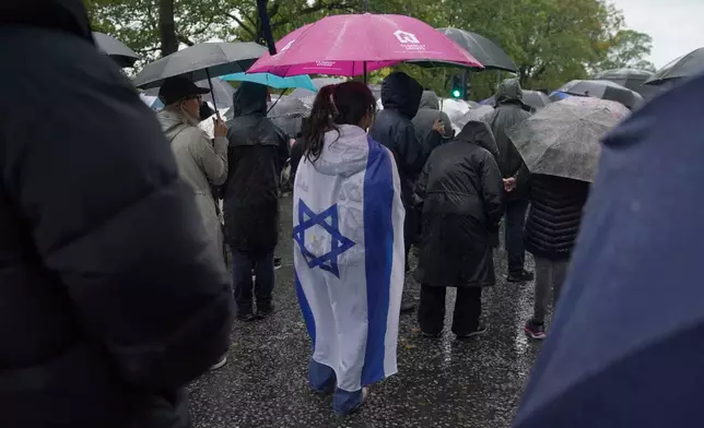 A woman wears the flag of Israel wrapped over her back as she attends a vigil for the victims of the attack on at Heaton Park Hebrew Congregation synagogue, in Crumpsall, Manchester, England, Friday, Oct. 3, 2025. (AP Photo/Ian Hodgson)