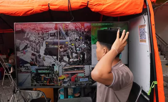 A student walks pas a TV screen showing the search efforts for the missing people of a building that collapsed at an Islamic boarding school in Sidoarjo, East Java, Indonesia, Saturday, Oct. 4, 2025. (AP Photo/Achmad Ibrahim)