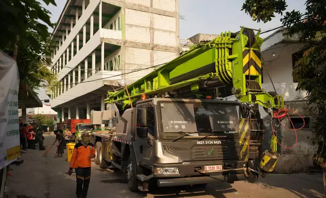A rescuer walks past a crane prepared for the search of missing people of a building that collapsed at an Islamic boarding school in Sidoarjo, East Java, Indonesia, Saturday, Oct. 4, 2025. (AP Photo/Achmad Ibrahim)