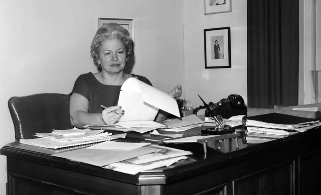 FILE - Liz Carpenter, press secretary and staff director for first lady Lady Bird Johnson, poses for a photo in her office in the East Wing of the White House in Washington, D.C., Dec. 9, 1963. On the walls are her Theta Sigma Phi Headliner Award and two photos of Mrs. Lyndon B. Johnson. (AP Photo/Harvey Georges, File)