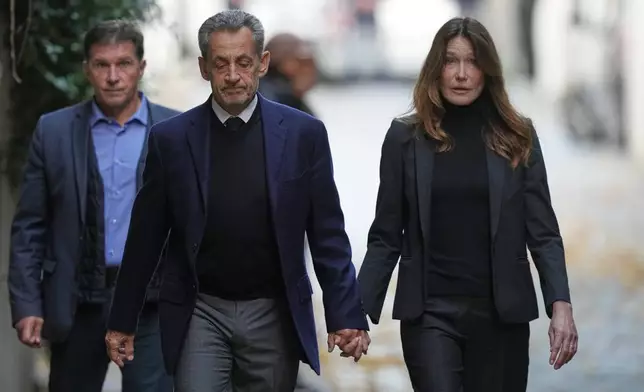 Former French President Nicolas Sarkozy and his wife Carla Bruni-Sarkozy leave their home Tuesday, Oct. 21, 2025 in Paris as Nicolas Sarkozy heads to prison to serve time for a criminal conspiracy to finance his 2007 election campaign with funds from Libya. (AP Photo/Thibault Camus)