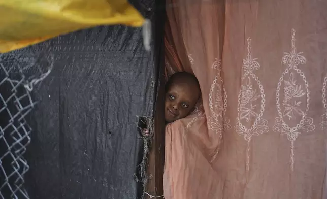 A child pokes his head out from behind a curtain at a shelter for families displaced by gang violence in Port-au-Prince, Haiti, Tuesday, Oct. 21, 2025. (AP Photo/Odelyn Joseph)