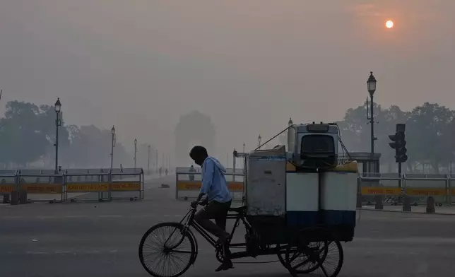 A cyclist pedals through morning smog near the India Gate monument as he transports used home appliances a day after Diwali festival in New Delhi, India, Tuesday, Oct. 21, 2025. (AP Photo/Manish Swarup)