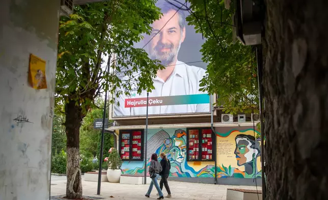 People walk beneath a political banner of the candidate for the mayor Hajrullah Ceku of the VeteVendosje (SelfDetermination) ahead of Sunday's municipal elections in capital Pristina, Saturday, Oct 11, 2025. (AP Photo/Visar Kryeziu)