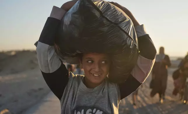 A displaced Palestinian girl carries a bag on her head as she walks along the coastal road near Wadi Gaza in the central Gaza Strip, heading toward Gaza City, Friday, Oct. 10, 2025, after Israel and Hamas agreed to a pause in their war and the release of the remaining hostages. (AP Photo/Abdel Kareem Hana)