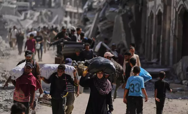 Displaced Palestinians walk with their belongings past destroyed buildings as they return to their homes in Khan Younis, southern Gaza Strip, Friday, Oct. 10, 2025, after Israel and Hamas agreed to a pause in their war and the release of the remaining hostages. (AP Photo/Jehad Alshrafi)