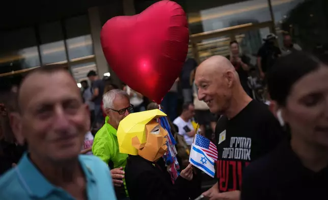 A person wears a mask depicting U.S. President Donald Trump as relatives and supporters of Israeli hostages held by Hamas in the Gaza Strip celebrate following the announcement that Israel and Hamas have agreed to the first phase of a peace plan to pause the fighting, as they gather at a plaza known as hostages square in Tel Aviv, Israel, Thursday, Oct. 9, 2025. (AP Photo/Emilio Morenatti)