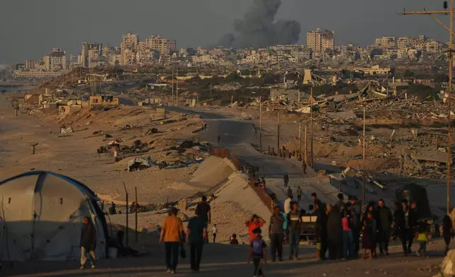 Displaced Palestinians walk along the coastal road, backdropped by smoke rising into the sky after an Israeli military strike in Gaza City, as seen from the central Gaza Strip, Wednesday, Oct. 8, 2025. (AP Photo/Abdel Kareem Hana)