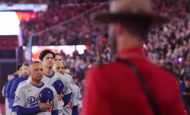 Los Angeles Dodgers manager Dave Roberts, left, two-way player Shohei Ohtani (17) and shortstop Mookie Betts (50) listen to the Canadian national anthem as Royal Canadian Mounted Police look on, ahead of the first inning Royal Canadian Mounted Police in Game 1 of baseball's World Series, Friday, Oct. 24, 2025, in Toronto. (Nathan Denette/The Canadian Press via AP)