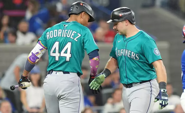 Seattle Mariners' Julio Rodríguez (44) congratulates teammate Cal Raleigh, right, as Raleigh crosses home plate after hitting a solo home run off Toronto Blue Jays pitcher Kevin Gausman during the sixth inning in Game 1 of baseball's American League Championship Series in Toronto, Sunday, Oct. 12, 2025. (Frank Gunn/The Canadian Press via AP)