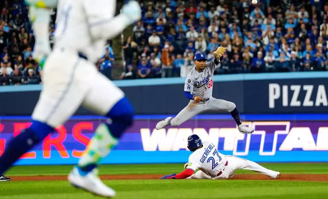 Los Angeles Dodgers shortstop Mookie Betts (50) puts out Toronto Blue Jays' Vladimir Guerrero Jr. (27) at second base as he throws to first to get out Bo Bichette, front left, for a third inning-ending double play during Game 1 of baseball's World Series in Toronto, Friday, Oct. 24, 2025. (Frank Gunn/The Canadian Press via AP)