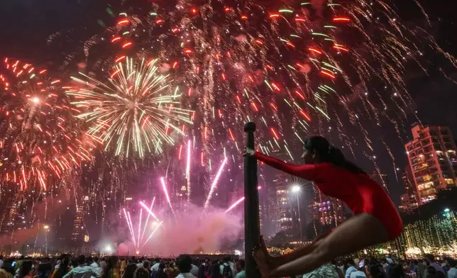 A girl performs on a mallakhamb pole as fireworks light up the sky during the festival of lights Diwali in Mumbai, India, on Monday, Oct. 20, 2025. (AP Photo/Rafiq Maqbool)